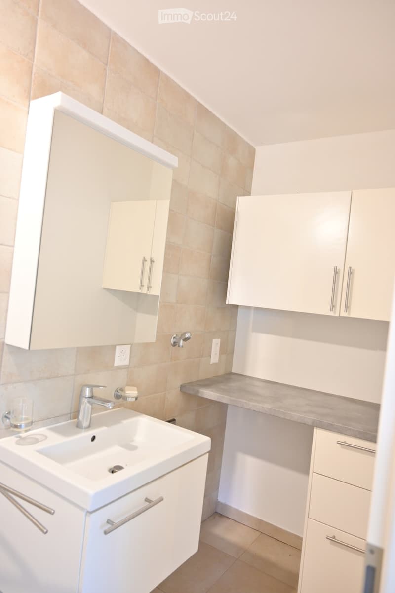Modern bathroom with white cabinets, a white sink, a mirror, and a glass cup on the counter.