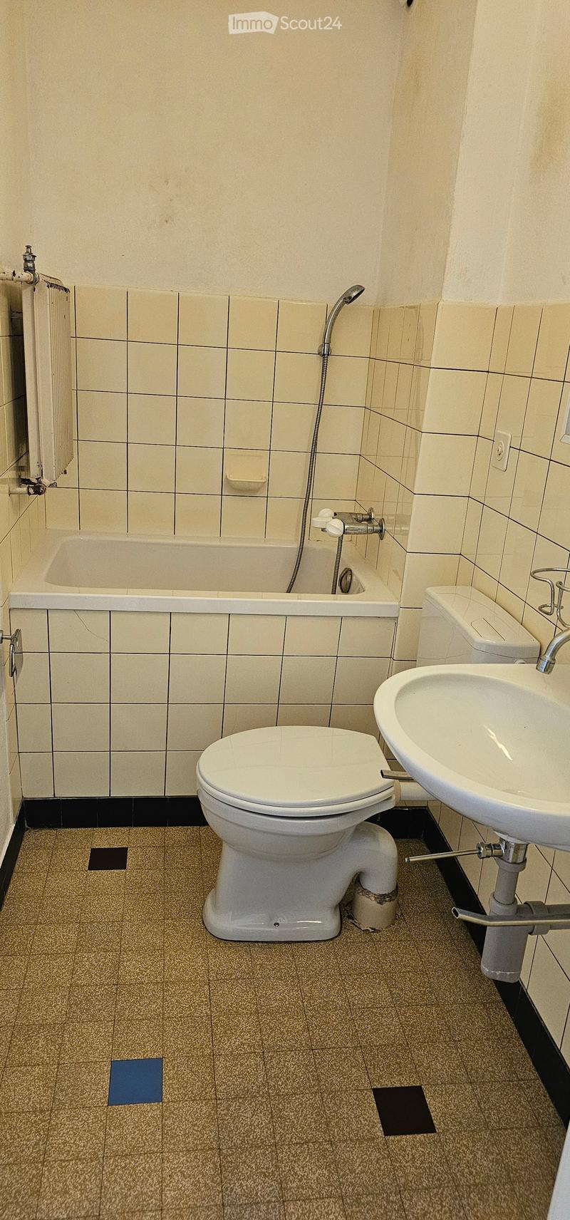 Bathroom with beige tiled walls, a white toilet, a sink, a bathtub, and a radiator. The floor is tiled with a speckled pattern.
