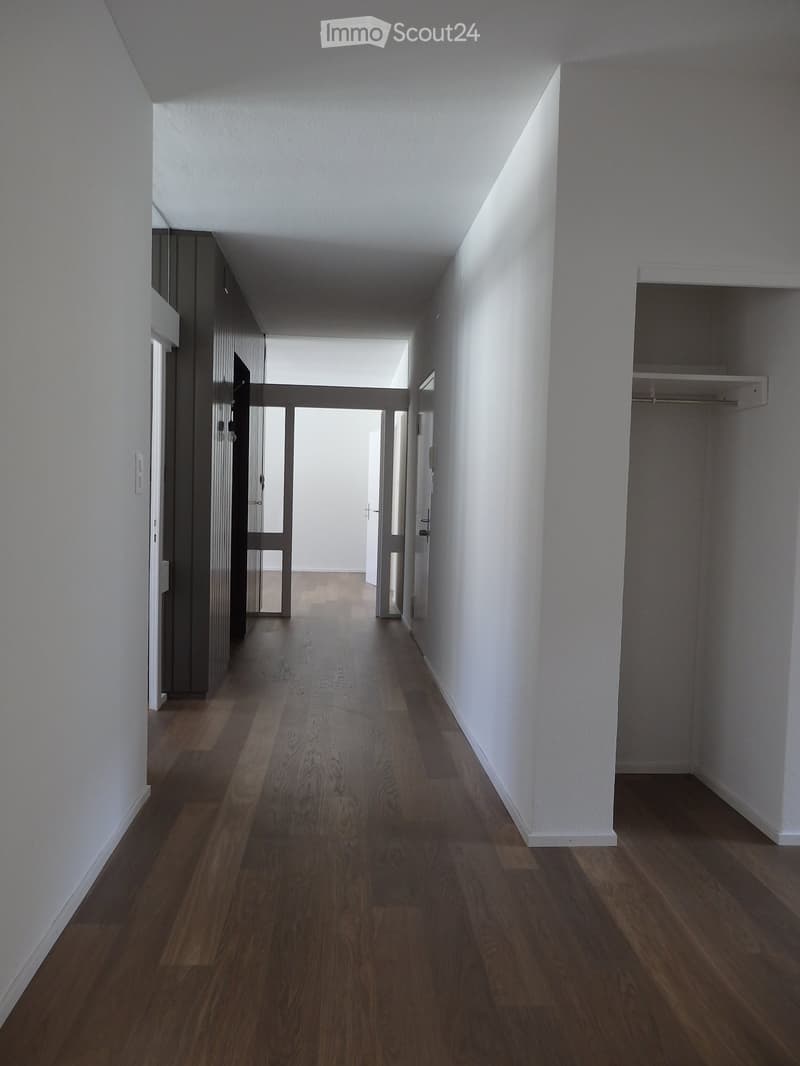 Empty hallway with wooden flooring, white walls, and doors leading to other rooms.