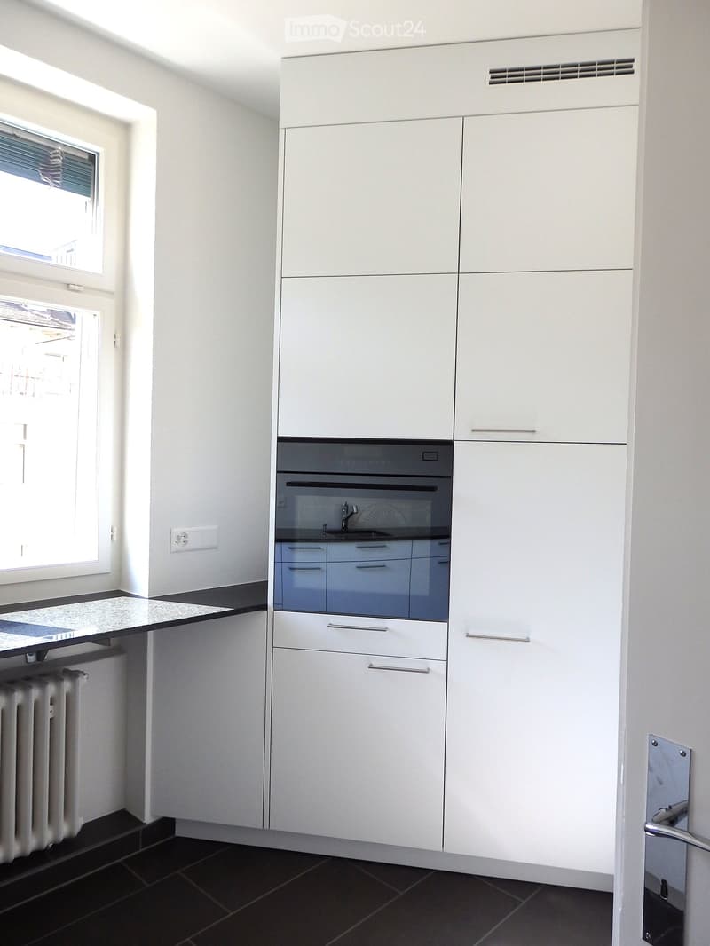 Modern kitchen with white cabinets, black countertops, and built-in oven. Features a window with blinds and a radiator under the window.