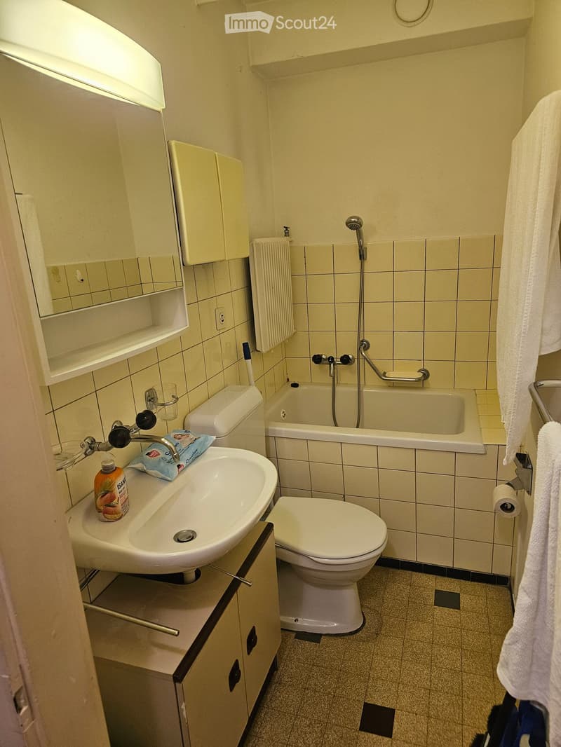 Compact bathroom with a sink, toilet, bathtub, mirror, and radiator. Includes a towel hanging on the side and a cup on the sink counter.