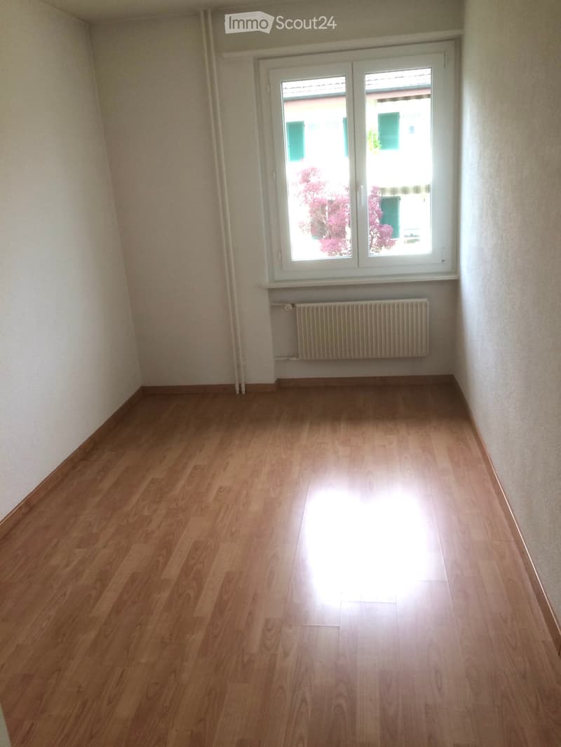 Empty room with wooden flooring, white walls, and a window with a radiator below it.