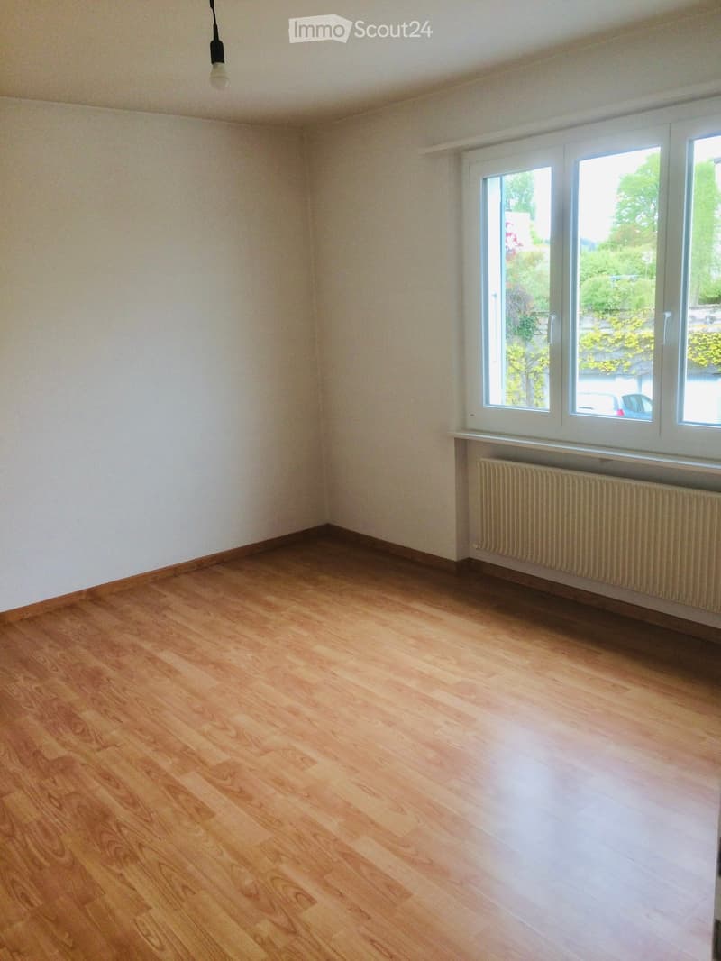 Empty room with wooden flooring, white walls, and large windows with a radiator below them.