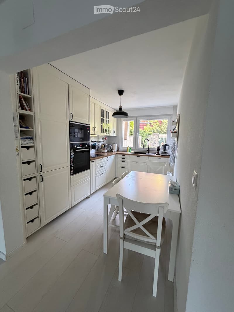 Bright kitchen with white cabinets, a central dining table with chairs, and modern appliances including an oven, microwave, and sink.