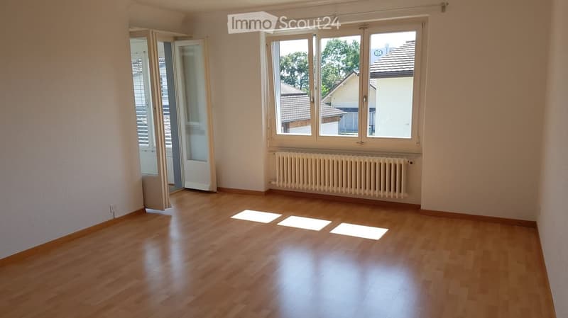 Empty room with wooden flooring, large windows, radiator, and open sliding door leading to a balcony.