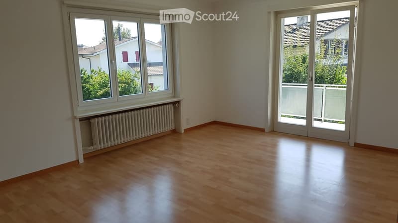 Empty room with wooden flooring, large windows, radiator, and sliding glass door leading to a balcony.