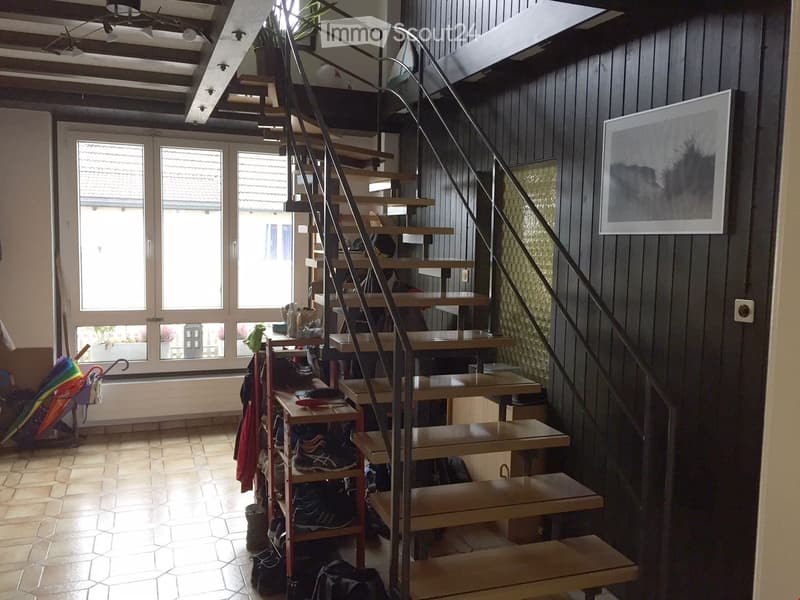 Hallway with a wooden staircase, shoe rack, and large windows letting in natural light.