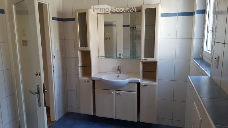 Modern bathroom with white tiles, a sink, a mirror, and built-in cabinets.
