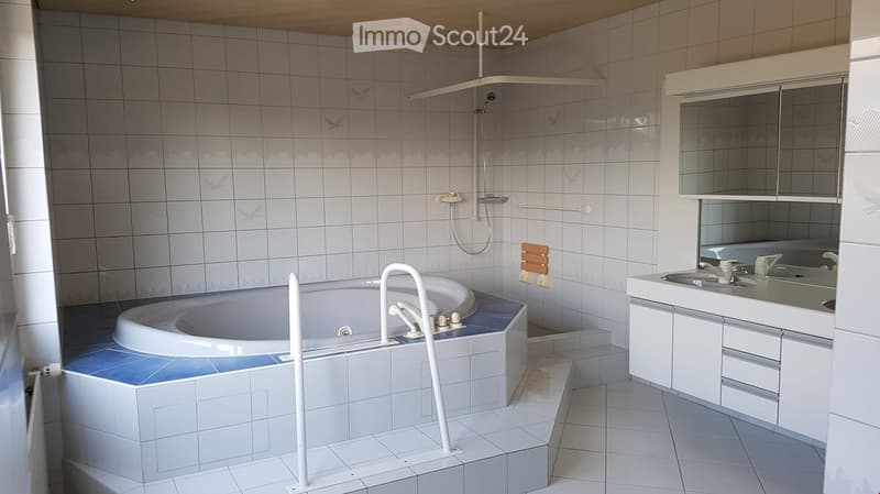 Modern bathroom with a large bathtub, double sink, mirror, and showerhead. The walls are tiled with a decorative pattern, and the floor is tiled in light gray.