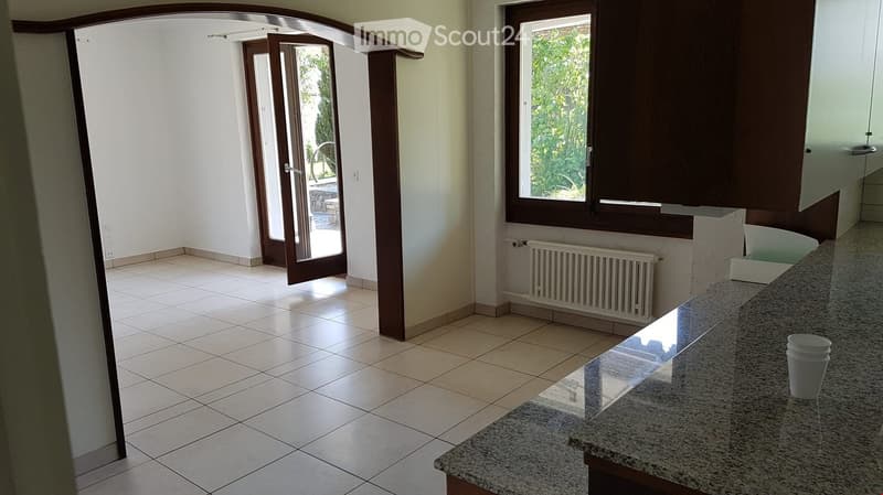 Empty room with tiled floor, white walls, a large window with a view of greenery, and a partially open sliding door leading outside.