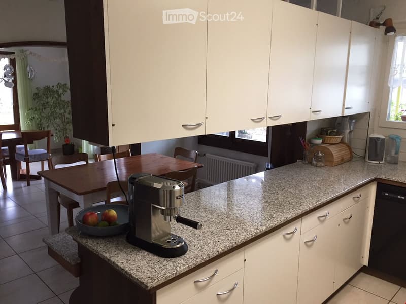 Modern kitchen with white cabinets, granite countertop, coffee maker, and a dining area with a wooden table and chairs.