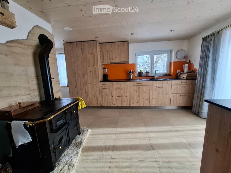 Modern kitchen with wooden cabinets, a black stove, a sink, and a window with a view of trees.