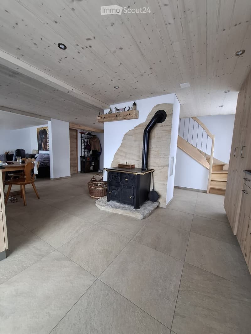 Cozy living space with a wood stove, wooden chair, table, basket, and staircase leading upwards.