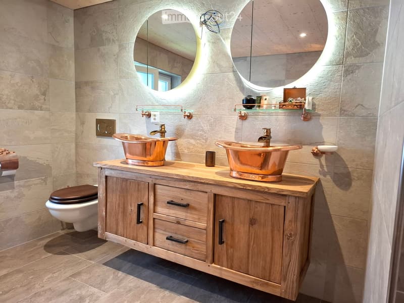 Elegant bathroom with two copper sinks, wooden vanity, large round mirrors, and a toilet.