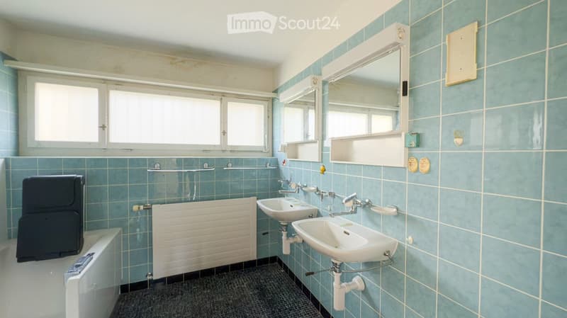 Bathroom with blue tiled walls and floor, featuring a bathtub, two sinks, a mirror, and a radiator.