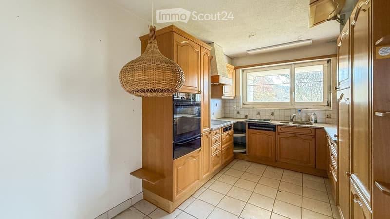 Bright kitchen with wooden cabinets, tiled floor, and a wicker pendant light. Features an oven, refrigerator, sink, and faucet.