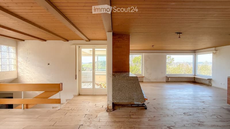 Empty room with wooden ceiling, large windows, and a concrete fireplace. No furniture or equipment present.