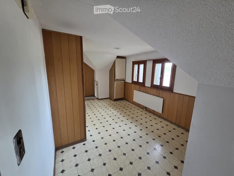 A narrow hallway with wooden paneling, white walls, and a patterned tile floor. Features include a radiator, a small cabinet, and three windows with wooden frames.