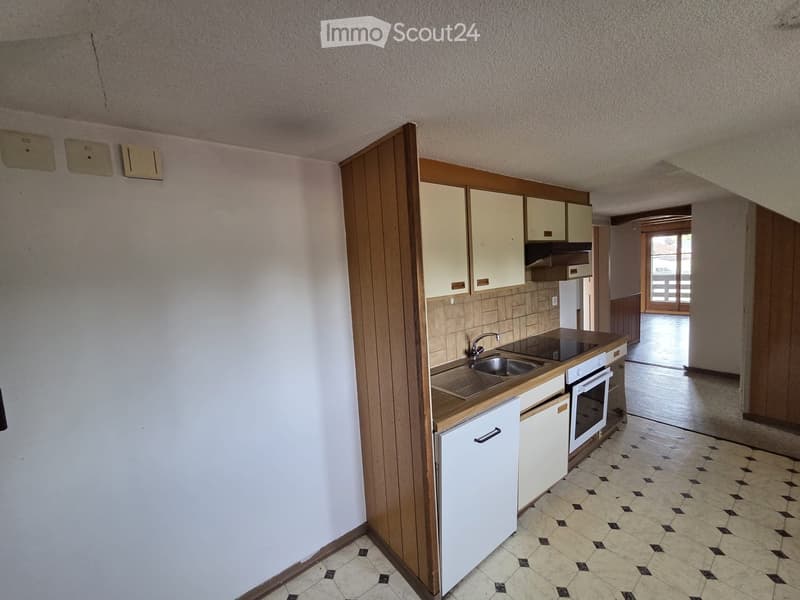 Compact kitchen with white cabinets, a sink, a faucet, and an oven. The floor is tiled with a black and beige pattern, and the walls are painted white.