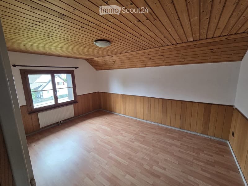 Empty room with wooden flooring, paneled walls, and a large window letting in natural light.