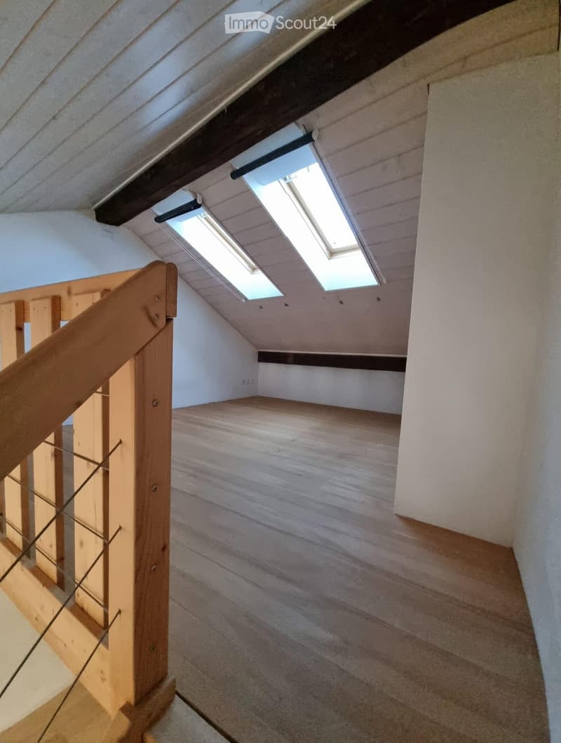 empty attic room with wooden floor, white walls, wooden railing, two skylights