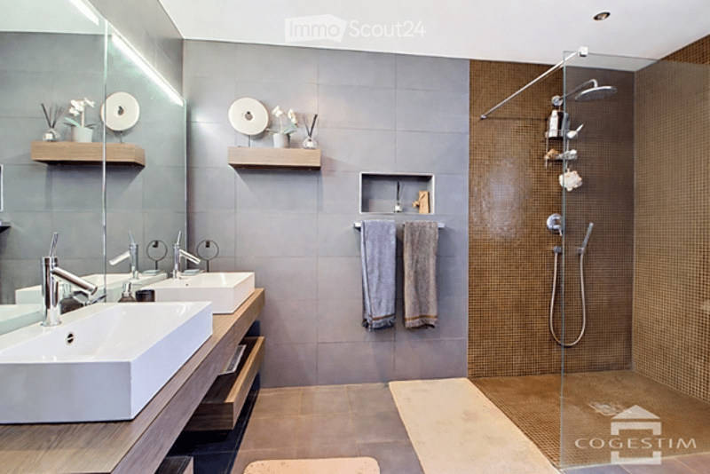 Modern bathroom with two white sinks, chrome faucets, a glass shower enclosure, and decorative shelves holding small vases and towels.