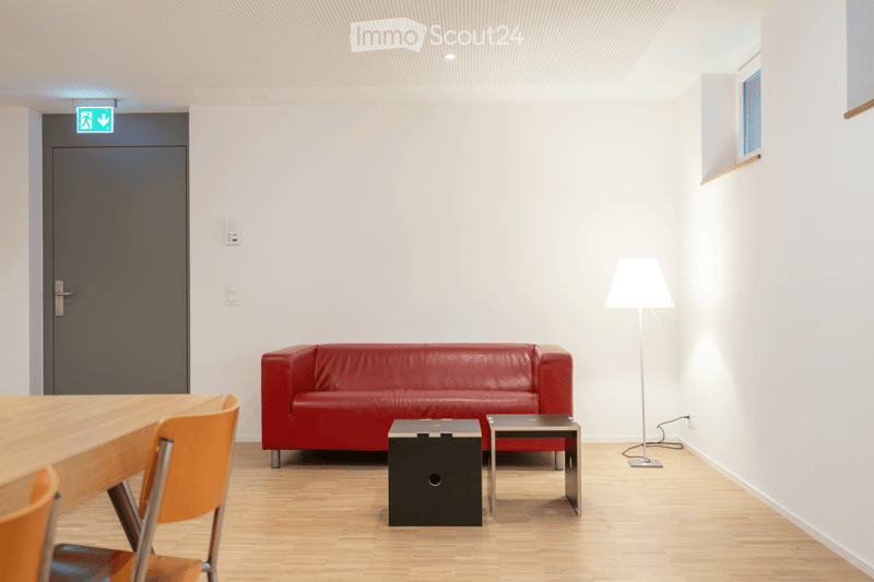 Modern living room with a red leather sofa, wooden table, orange chairs, and a floor lamp.