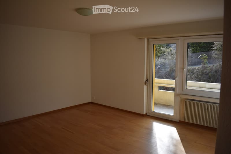 Empty room with wooden flooring, white walls, large window, and sliding glass door leading to a balcony.