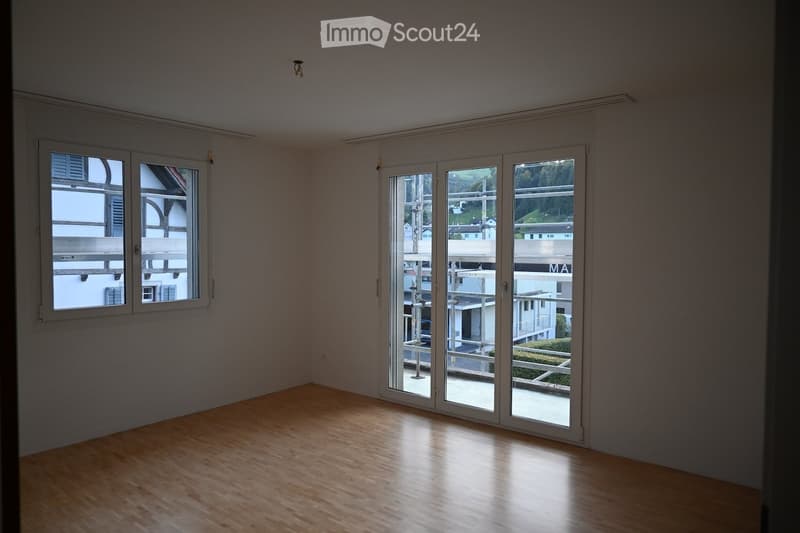 Spacious room with wooden floors, sliding glass doors leading to balcony, two windows