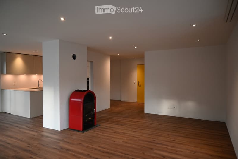 large empty room, red fireplace, hardwood floors, white walls, kitchen area, power outlets
