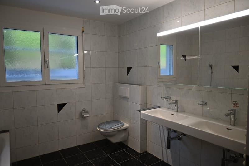 Modern bathroom with white tiles, double sink, modern shower, toilet and small bathtub.