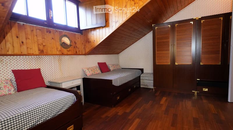 Cozy bedroom with wooden walls and ceiling, two single beds with checkered bedding, nightstand, mirror, and built-in wardrobe with louvered doors.