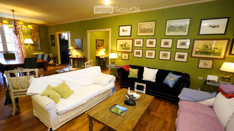 Living room with green walls, wooden floor, two sofas, coffee table, chairs, lamps, and framed pictures on the wall.