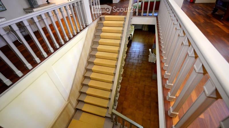 Spacious hallway with wooden floors, white railings, and yellow carpeted stairs leading upwards.