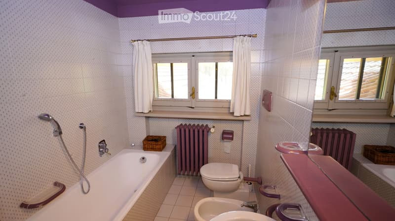Bathroom with a bathtub, toilet, sink, radiator, showerhead, wicker baskets, and a mirror. The room features white tiled walls and a purple accent color on fixtures and radiator covers.