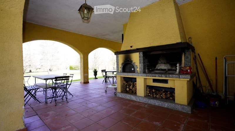 Outdoor patio with a large brick oven, tiled floor, and several tables and chairs arranged for seating.