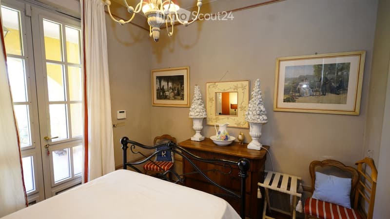 Elegant bedroom with a metal-framed bed, wooden nightstand, decorative vases, framed artwork, and a window with white curtains.