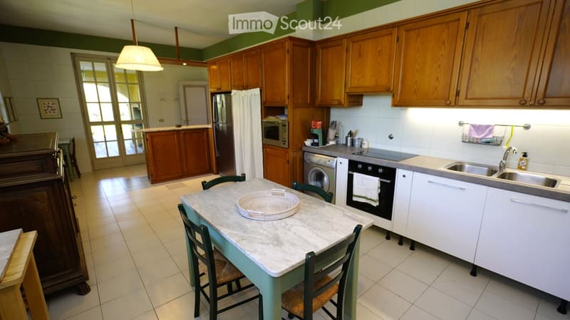 Bright kitchen with wooden cabinets, marble countertop, and stainless steel appliances. Includes a dining table with chairs, sink, and various kitchen items.