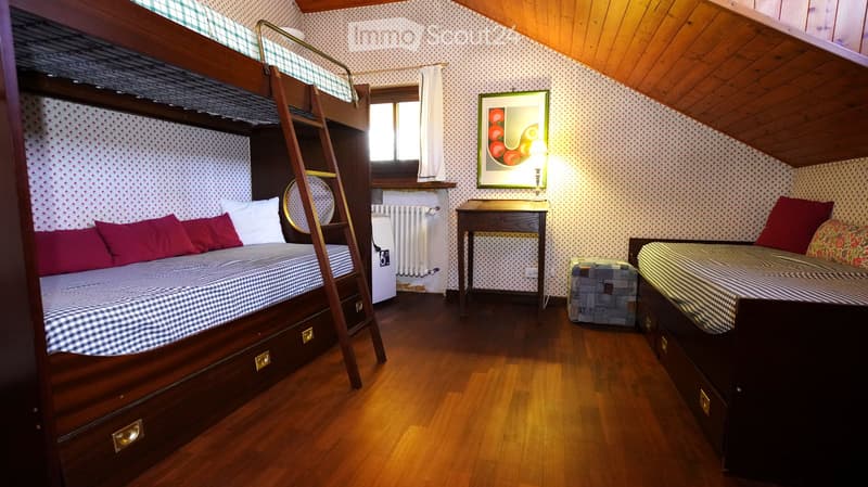 Cozy bedroom with wooden floors, bunk bed, small table, chair, radiator, picture frame, and additional bed with nightstand and drawer.