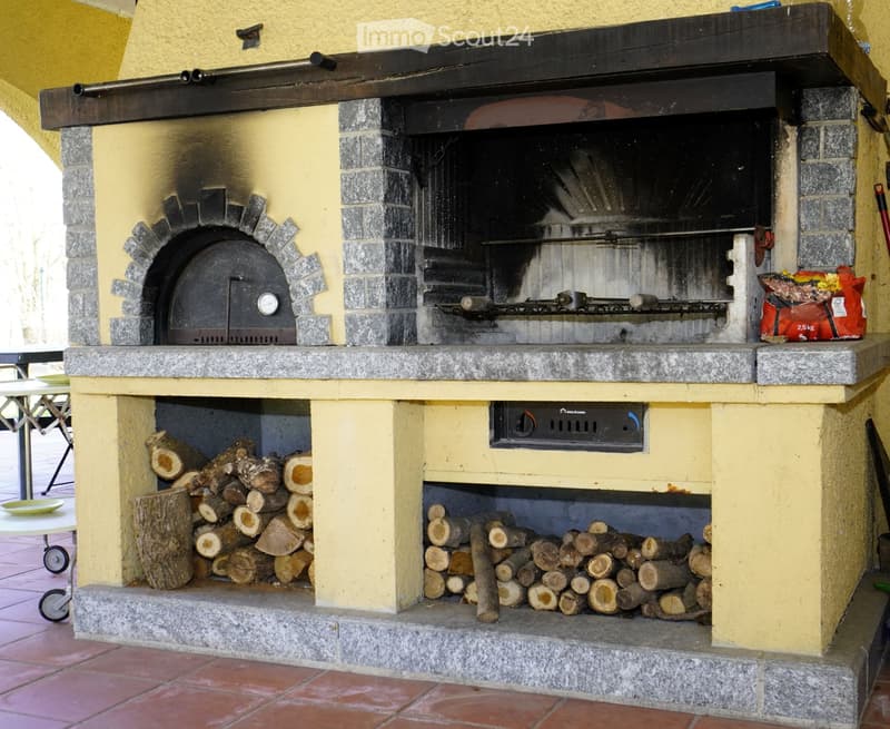 Outdoor area with a stone pizza oven, wood storage, and a small table with plates.