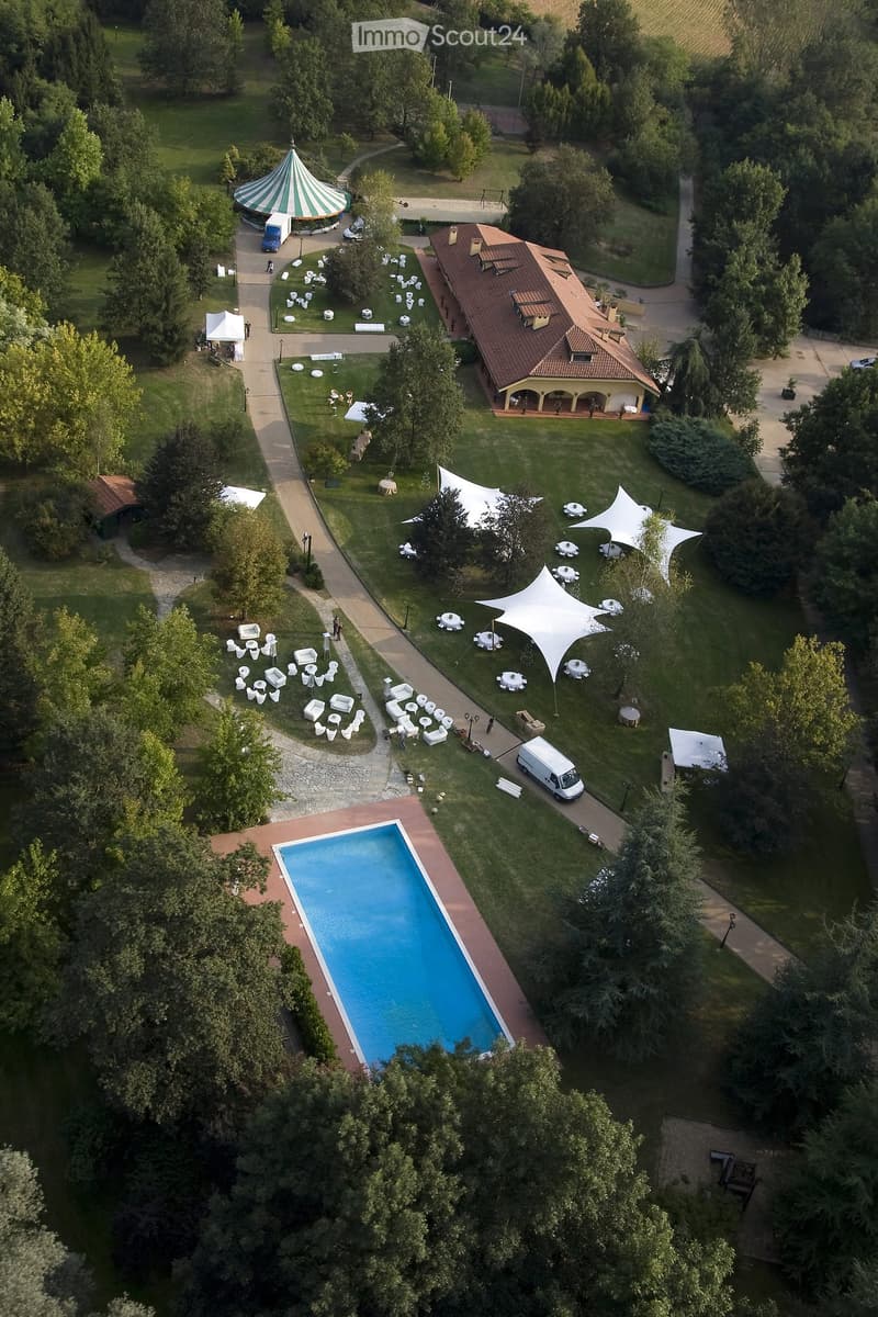 Aerial view of a large outdoor area with a swimming pool, several tents, and scattered chairs and tables, surrounded by trees and pathways.