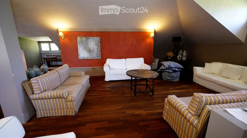 Living room with wooden flooring, white and striped sofas, coffee table, side table, decorative vases, and wall-mounted lamps.