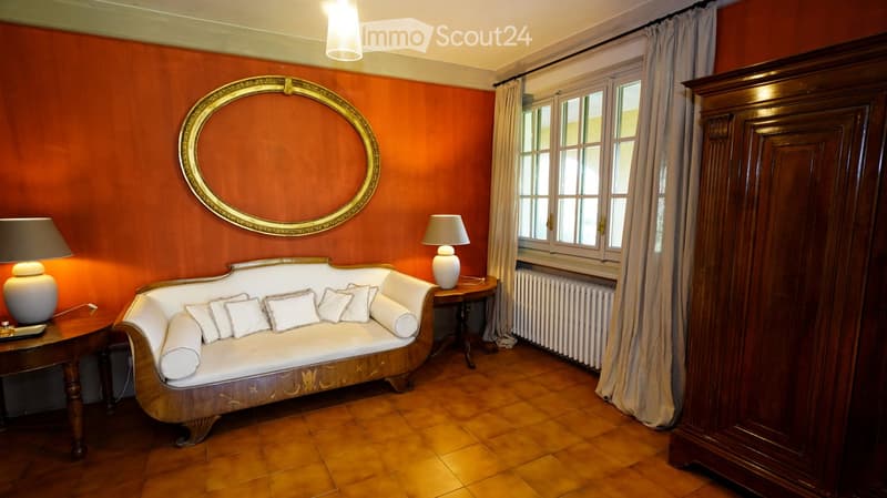 Elegant living room with a white sofa, wooden cabinet, and decorative mirror on orange walls.