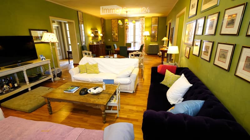 Living room with green walls, wooden floor, white sofa, dark blue sofa, coffee table, chairs, lamps, and framed pictures on the walls.