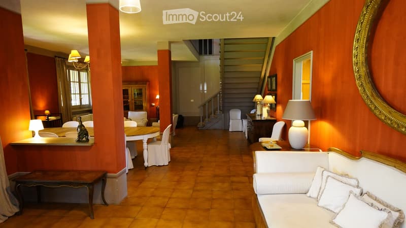 Elegant living area with warm orange walls, wooden flooring, and classic furniture including a sofa, dining table, chairs, lamps, and a decorative statue.