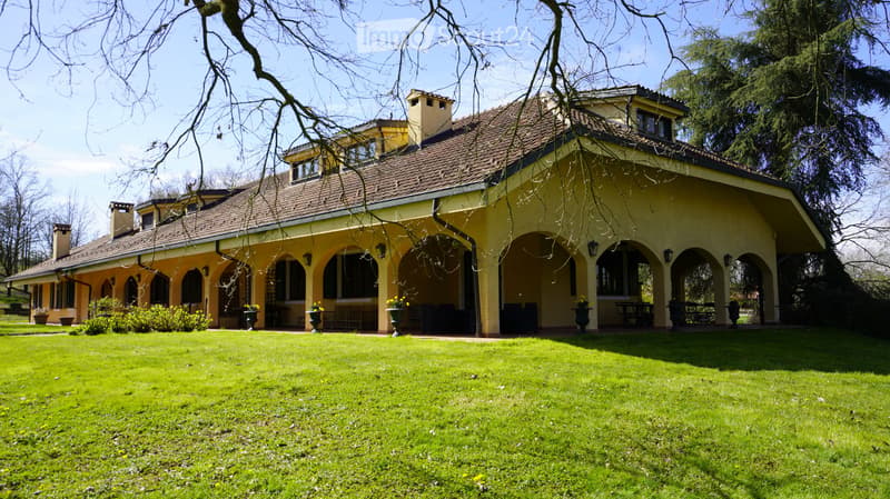 Two-story yellow house with a tiled roof, arched porch, and well-maintained lawn.