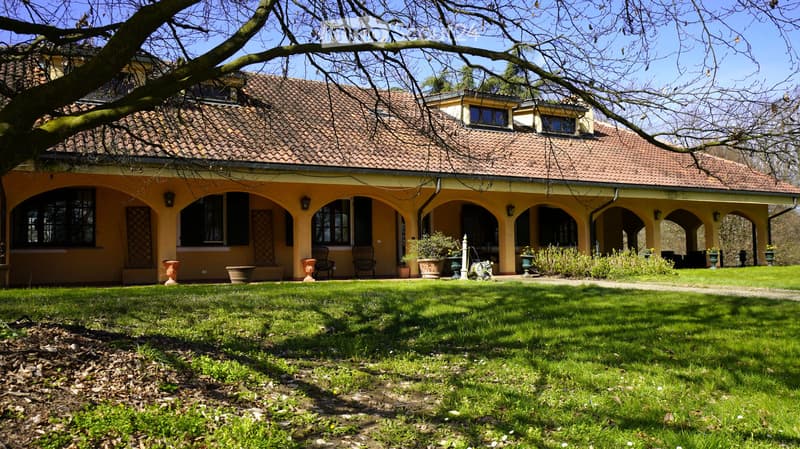 A two-story house with a tiled roof and arched windows, surrounded by a well-maintained lawn and garden.