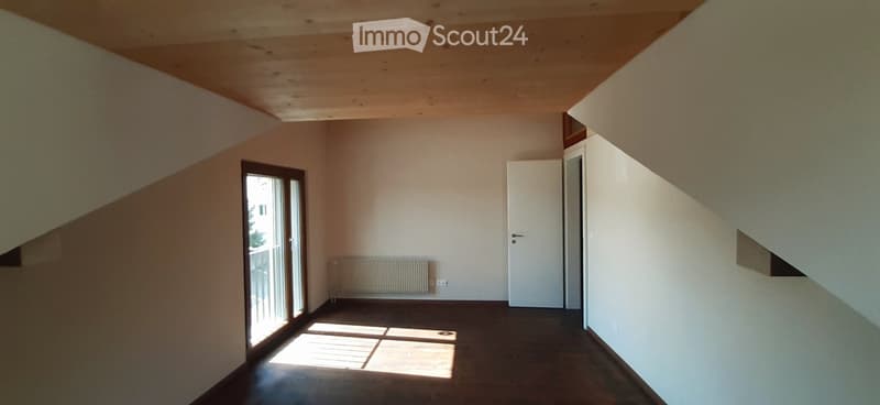 Spacious room with wooden ceiling, large window, and radiator. The room has a minimalist and clean design.