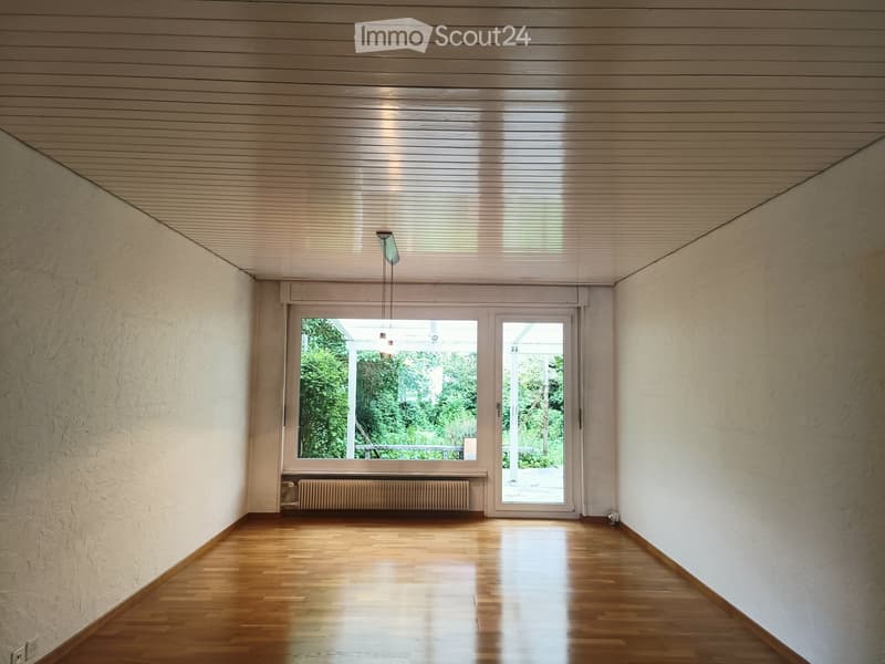 Empty room with wooden flooring, white walls, large window and door leading outside, radiator, and a hanging light fixture.