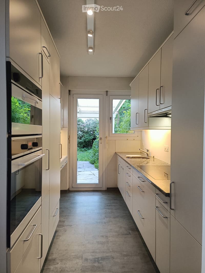 Modern kitchen with white cabinets, stainless steel appliances, and a large window overlooking a garden.